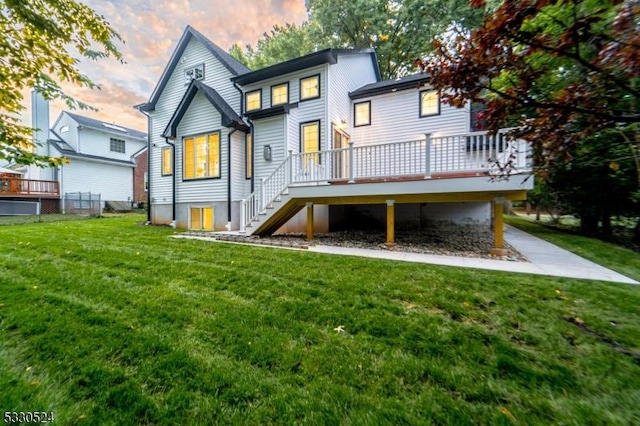 back house at dusk with a lawn and a deck