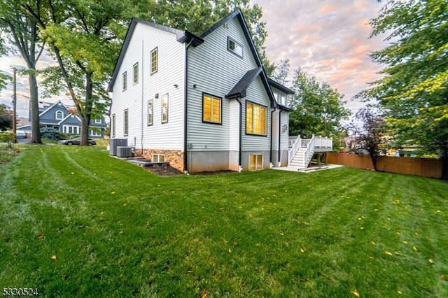 back house at dusk featuring a wooden deck, a yard, and central air condition unit