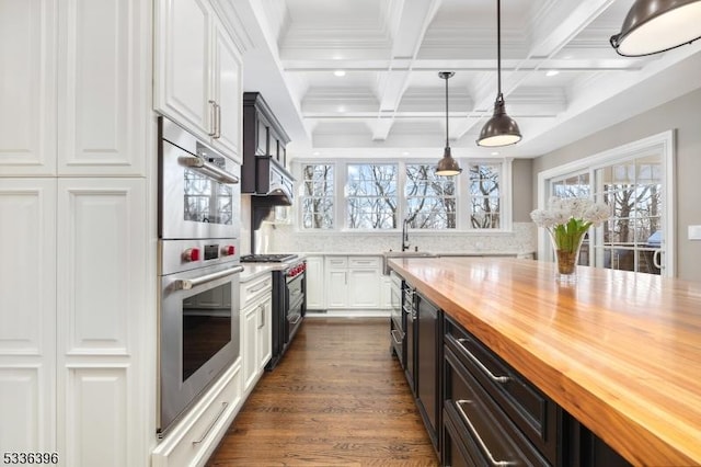 kitchen with beam ceiling, stainless steel appliances, wooden counters, white cabinets, and plenty of natural light