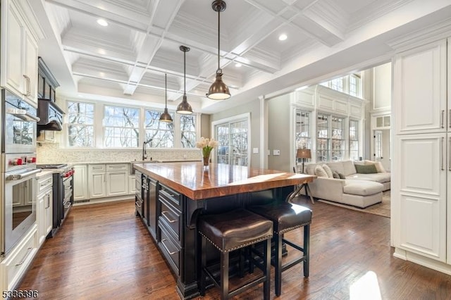 kitchen featuring butcher block counters, a breakfast bar, beamed ceiling, stainless steel appliances, and white cabinetry