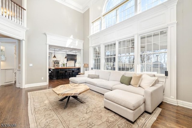 living room with a towering ceiling, baseboards, ornamental molding, and dark wood-style flooring