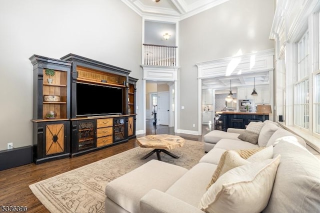 living area featuring a high ceiling, coffered ceiling, wood finished floors, baseboards, and crown molding