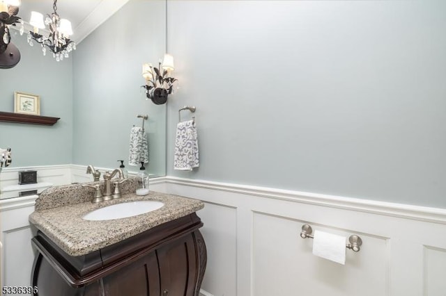 bathroom featuring a wainscoted wall, a notable chandelier, vanity, and a decorative wall