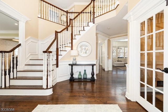 entrance foyer featuring ornamental molding, a decorative wall, a towering ceiling, and wood finished floors