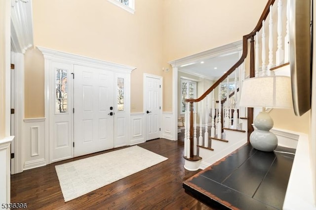 entrance foyer with a wainscoted wall, a high ceiling, wood finished floors, and a decorative wall