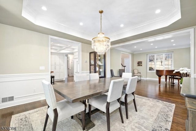 dining room featuring a tray ceiling, visible vents, wood finished floors, and wainscoting