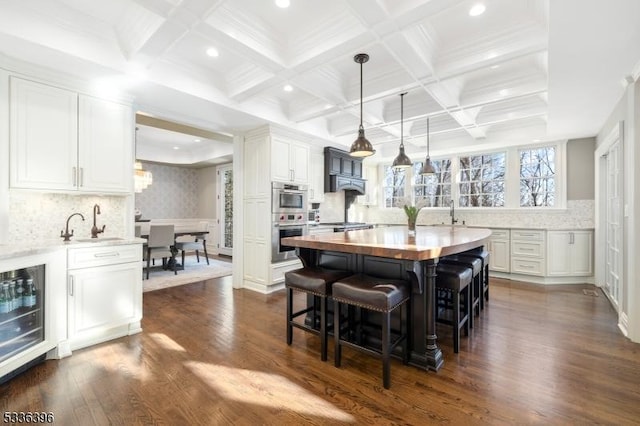 kitchen with dark wood-style floors, a breakfast bar area, butcher block counters, white cabinets, and beamed ceiling