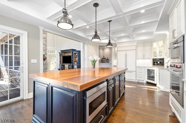 kitchen with built in appliances, wine cooler, butcher block countertops, white cabinetry, and beamed ceiling