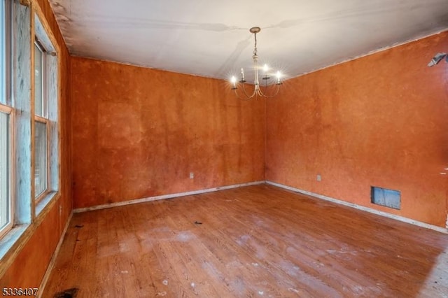 empty room with wood-type flooring and a chandelier