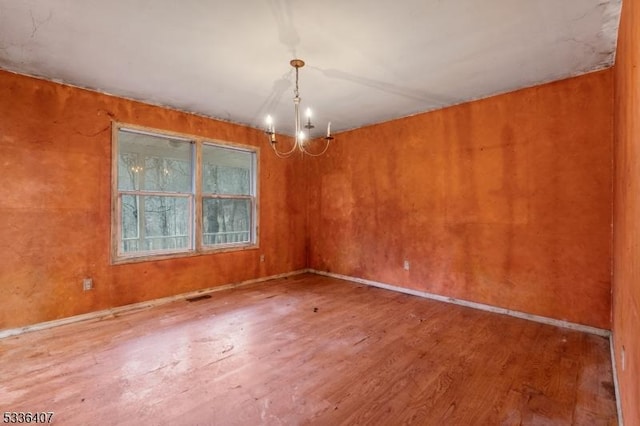 spare room with an inviting chandelier and hardwood / wood-style flooring