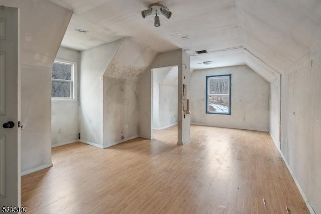 additional living space with light hardwood / wood-style flooring, a healthy amount of sunlight, and vaulted ceiling