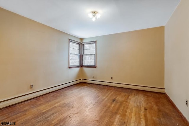 unfurnished room with a baseboard heating unit and wood-type flooring