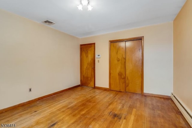 unfurnished bedroom featuring baseboard heating, a closet, and light hardwood / wood-style flooring