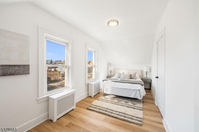 bedroom with vaulted ceiling, radiator, and light hardwood / wood-style floors