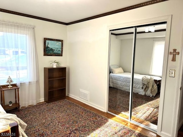 bedroom featuring multiple windows, crown molding, dark hardwood / wood-style flooring, and a closet