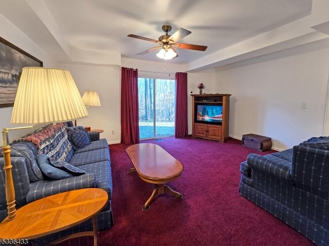 living room with dark colored carpet, ceiling fan, and a tray ceiling