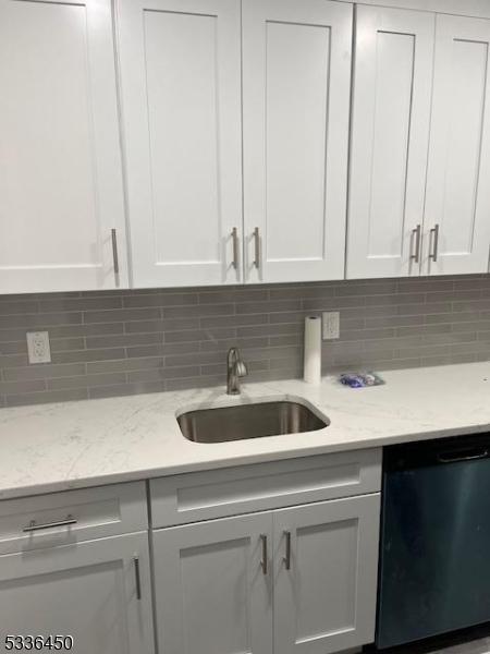 kitchen with tasteful backsplash, white cabinetry, sink, and dishwashing machine