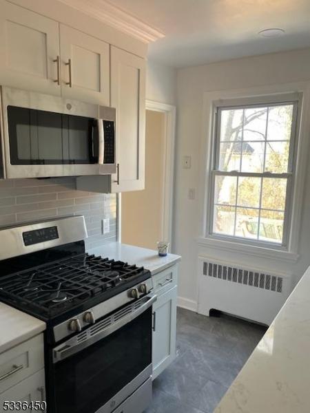 kitchen featuring stainless steel appliances, radiator, white cabinets, and decorative backsplash