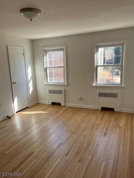 unfurnished room with light hardwood / wood-style flooring and radiator heating unit