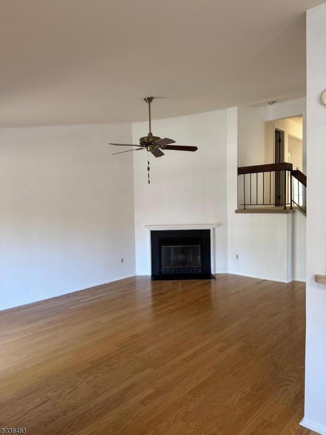 unfurnished living room with wood finished floors, a fireplace with flush hearth, and a ceiling fan