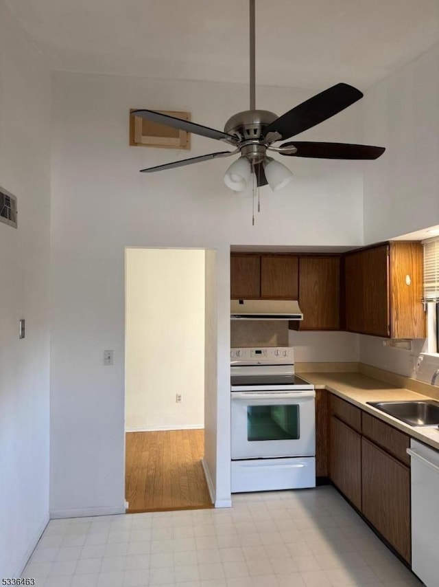 kitchen with under cabinet range hood, white appliances, a sink, light countertops, and light floors