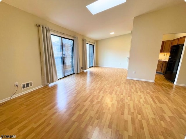 empty room featuring sink, a skylight, and light hardwood / wood-style floors