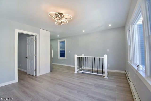 empty room featuring an inviting chandelier, light hardwood / wood-style flooring, and a baseboard heating unit