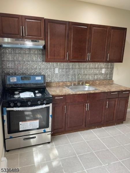 kitchen featuring under cabinet range hood, a sink, light countertops, stainless steel gas stove, and tasteful backsplash