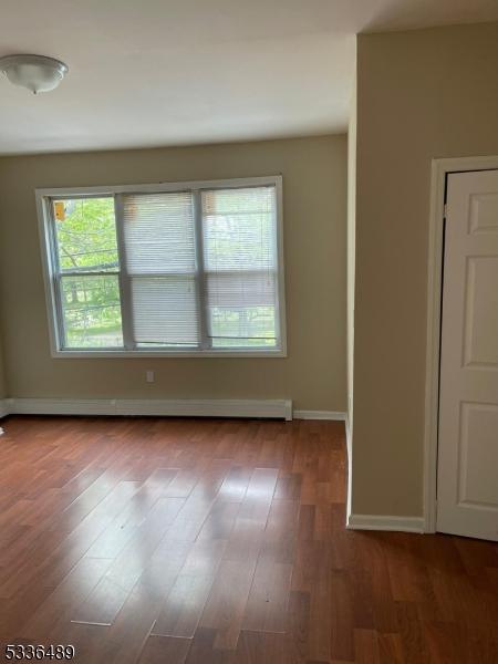 empty room with baseboards, a baseboard heating unit, and wood finished floors