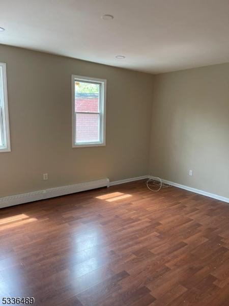 empty room featuring a baseboard radiator, wood finished floors, and baseboards