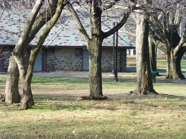 obstructed view of property featuring stone siding, a high end roof, and a front yard