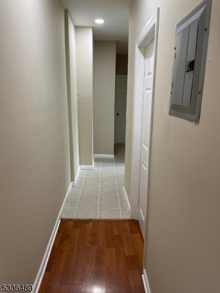 hall with wood finished floors, electric panel, and baseboards