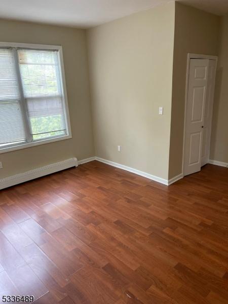 empty room with a baseboard radiator, wood finished floors, and baseboards