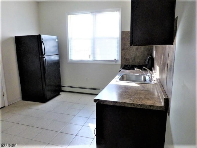 kitchen with light tile patterned floors, a baseboard radiator, a sink, backsplash, and freestanding refrigerator