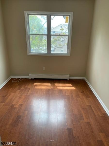 unfurnished room with a baseboard heating unit, plenty of natural light, baseboards, and wood finished floors