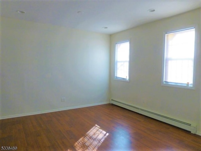 empty room with baseboards, a baseboard heating unit, and wood finished floors