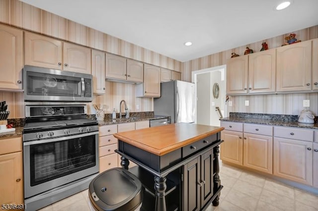 kitchen with stainless steel appliances, sink, light brown cabinetry, and dark stone counters