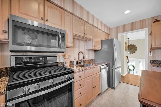 kitchen with stainless steel appliances, light brown cabinetry, sink, and dark stone counters