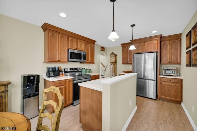 kitchen featuring sink, light hardwood / wood-style flooring, appliances with stainless steel finishes, a kitchen island with sink, and hanging light fixtures