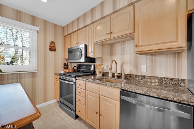 kitchen with stainless steel appliances, light brown cabinetry, sink, and dark stone countertops