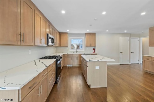 kitchen with light stone counters, appliances with stainless steel finishes, a center island, and hardwood / wood-style floors