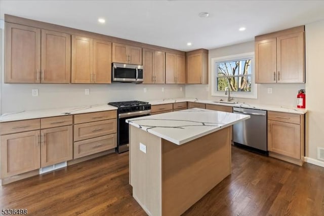 kitchen with sink, appliances with stainless steel finishes, dark hardwood / wood-style flooring, a kitchen island, and light stone countertops