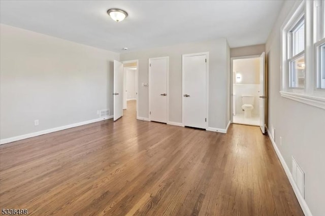 unfurnished bedroom featuring connected bathroom and hardwood / wood-style floors