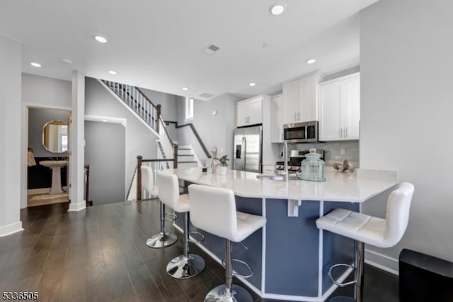 kitchen featuring a breakfast bar area, white cabinetry, tasteful backsplash, dark hardwood / wood-style floors, and stainless steel appliances