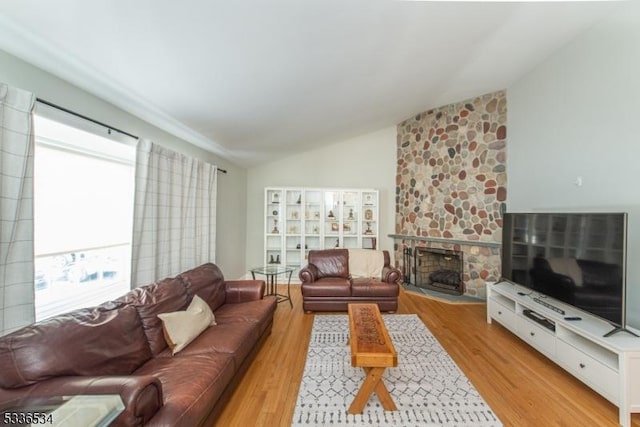 living room with vaulted ceiling, a fireplace, and light hardwood / wood-style flooring