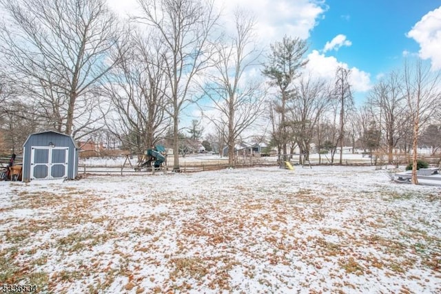 snowy yard featuring a playground and a shed