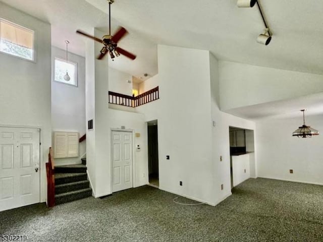 unfurnished living room with ceiling fan, high vaulted ceiling, rail lighting, and dark carpet