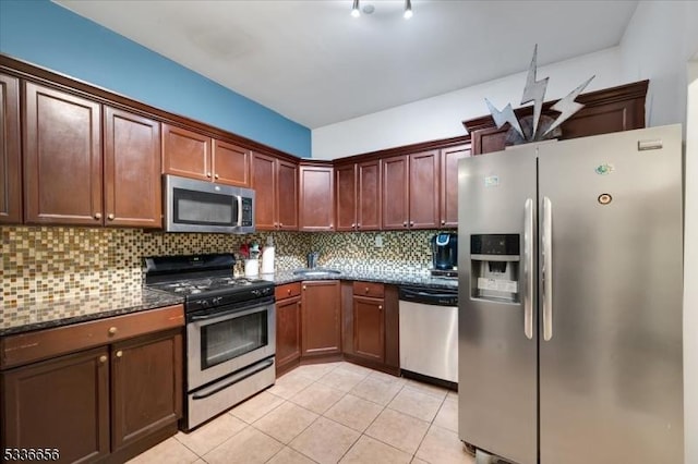 kitchen featuring sink, dark stone countertops, stainless steel appliances, tasteful backsplash, and light tile patterned flooring