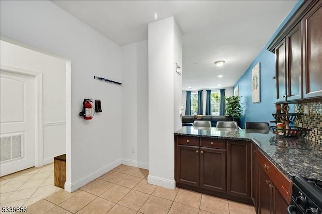 kitchen with light tile patterned flooring, kitchen peninsula, decorative backsplash, and dark stone countertops