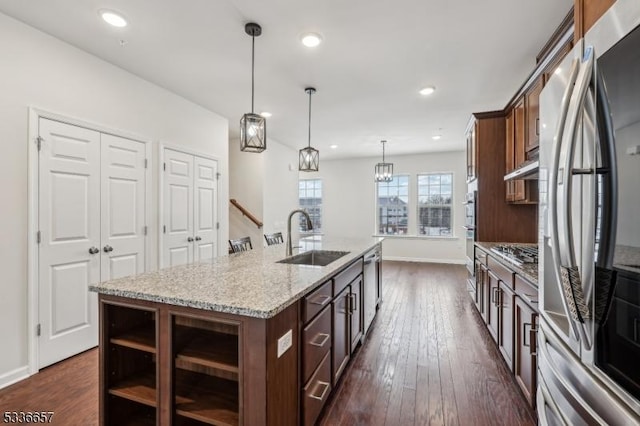 kitchen featuring sink, light stone counters, hanging light fixtures, a center island with sink, and appliances with stainless steel finishes